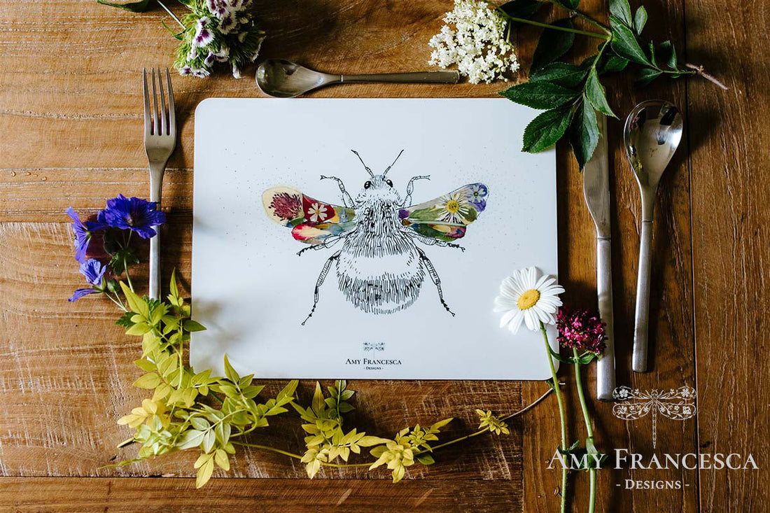 Product visualisation showing a placemat with a bee illustration, surrounded by flowers and cutlery on a wooden table.