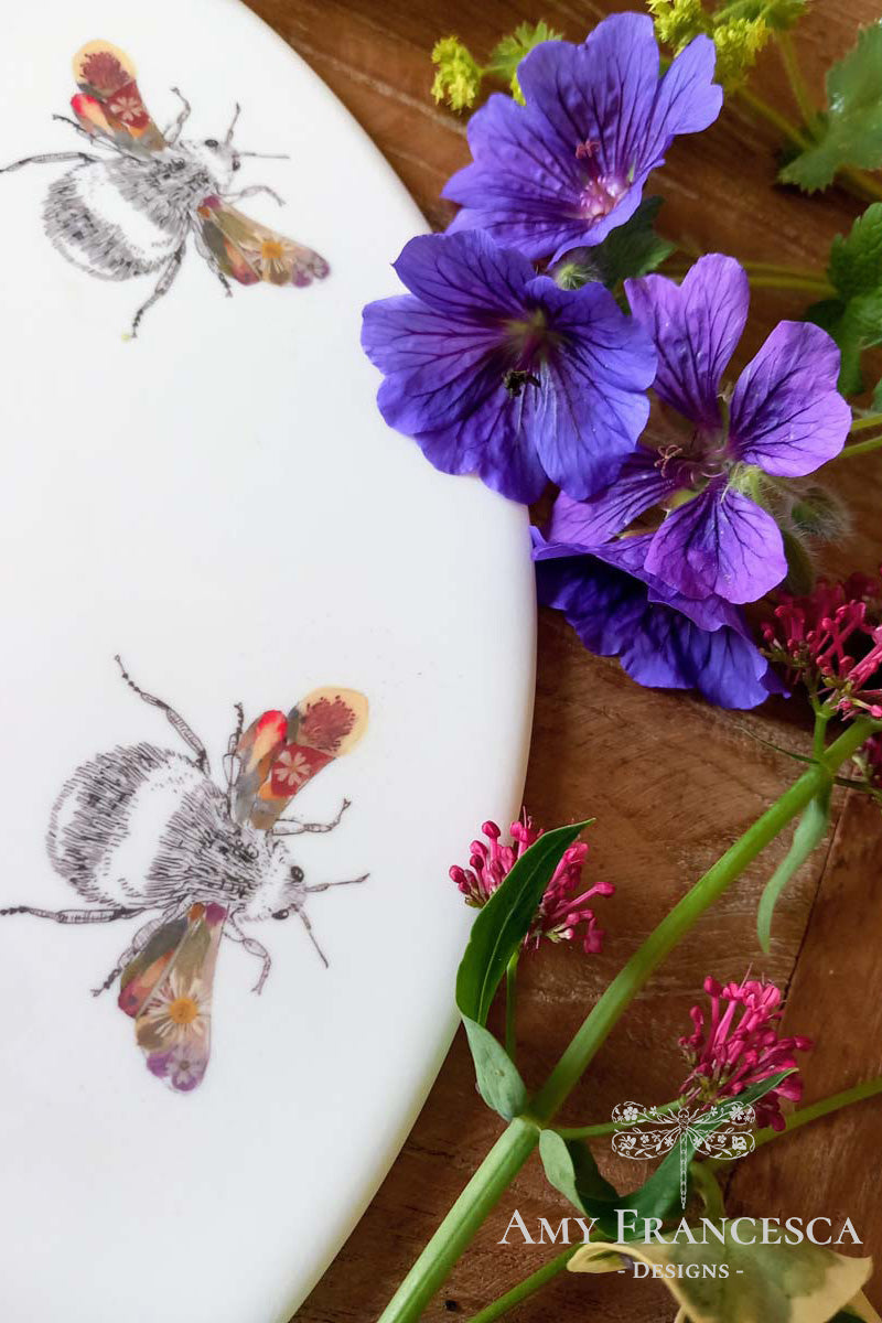 Serving platter featuring bee illustrations, shown with surrounding flowers.