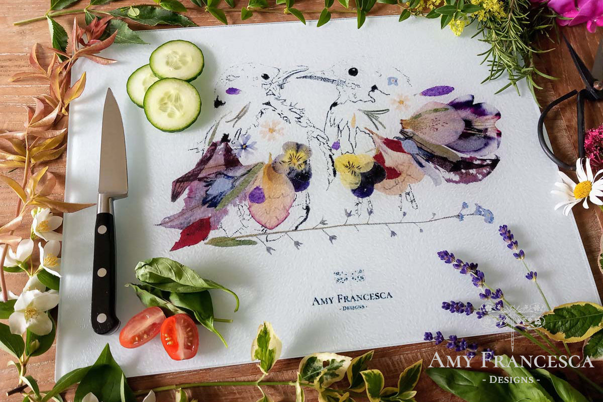 Chopping board featuring two bird illustrations, shown with sliced vegetables and herbs.