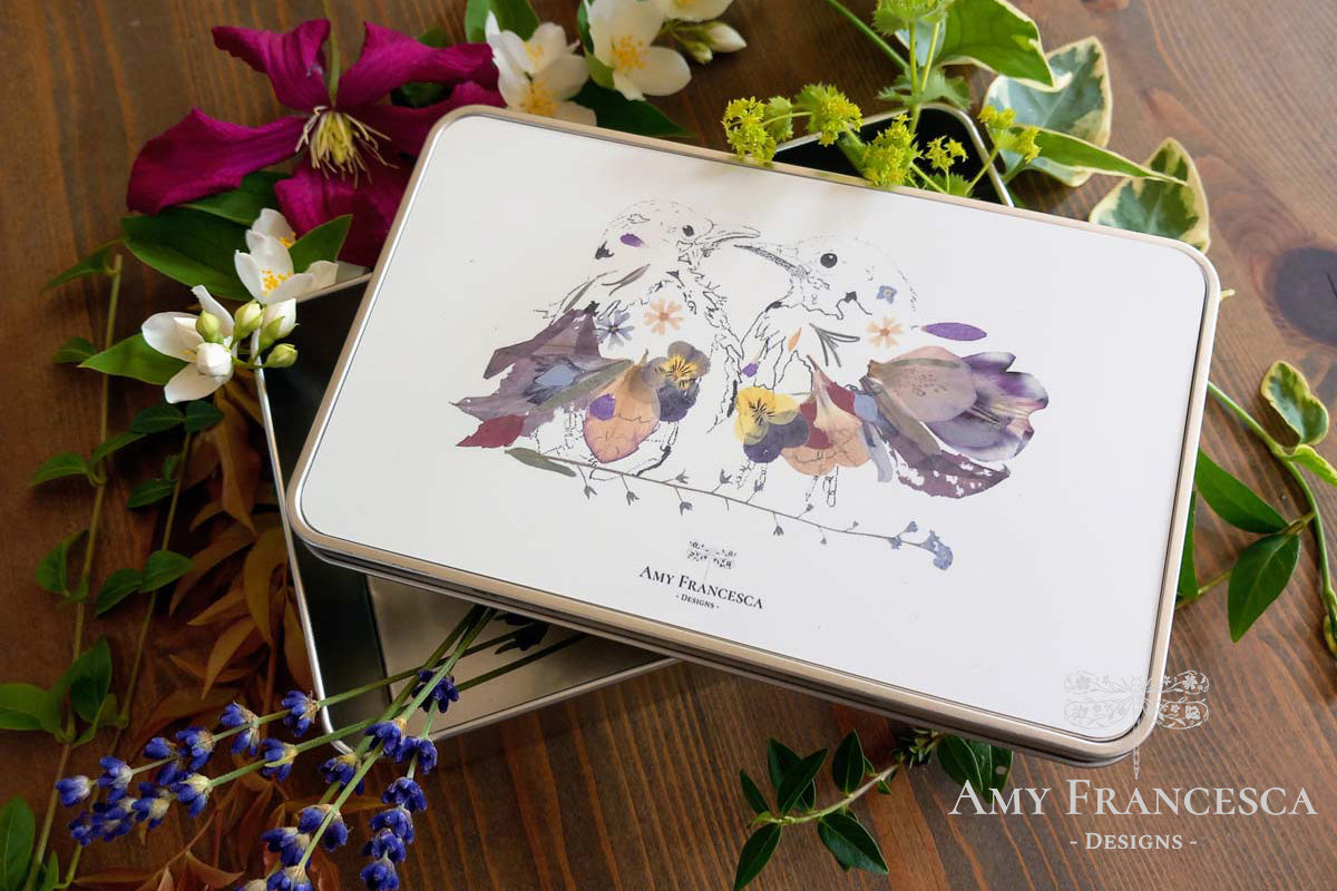 Rectangular storage tin featuring two bird illustrations, shown with surrounding flowers and foliage.