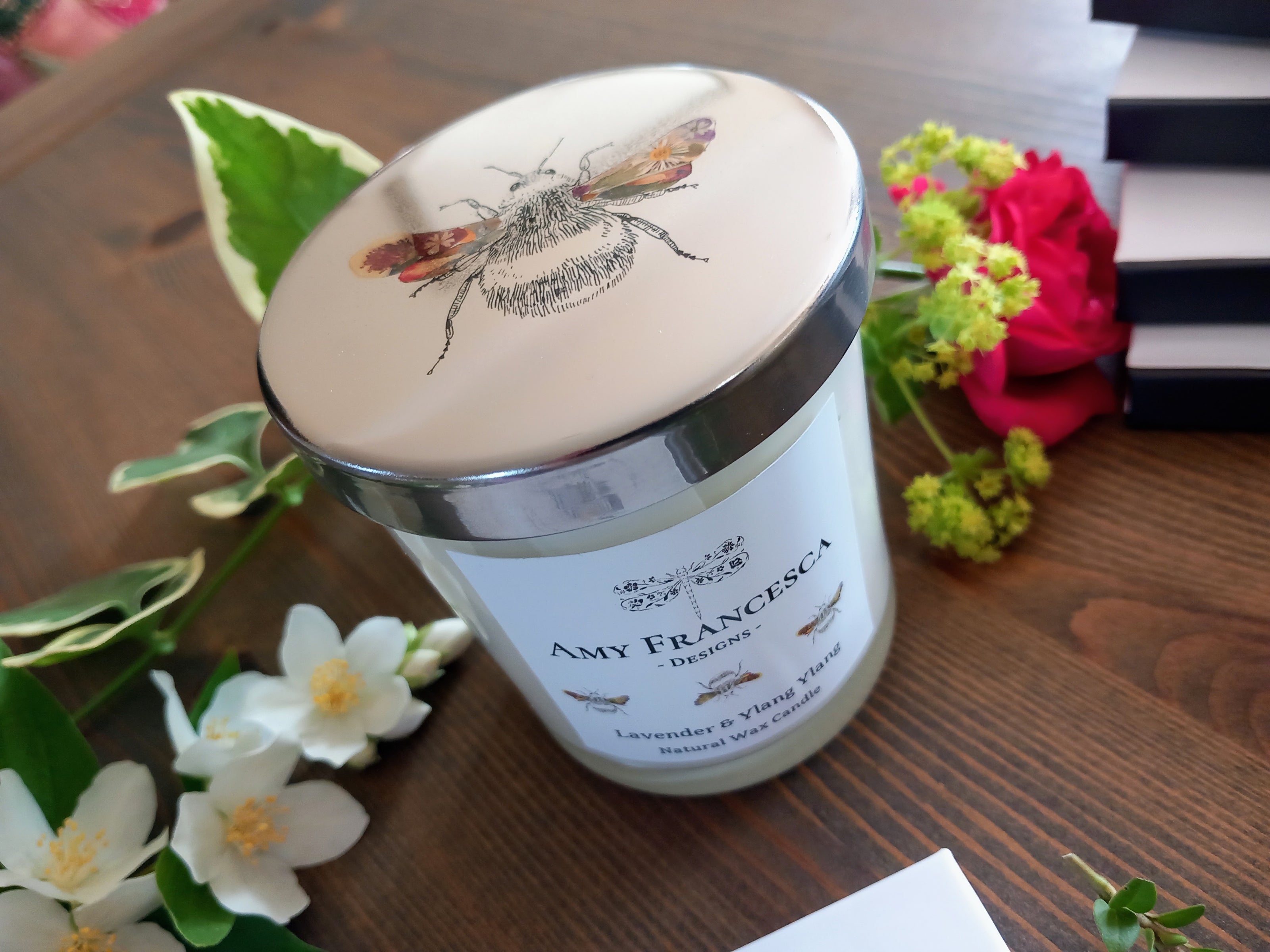 Candle featuring bee illustrations on both the lid and the jar label, shown with surrounding flowers.