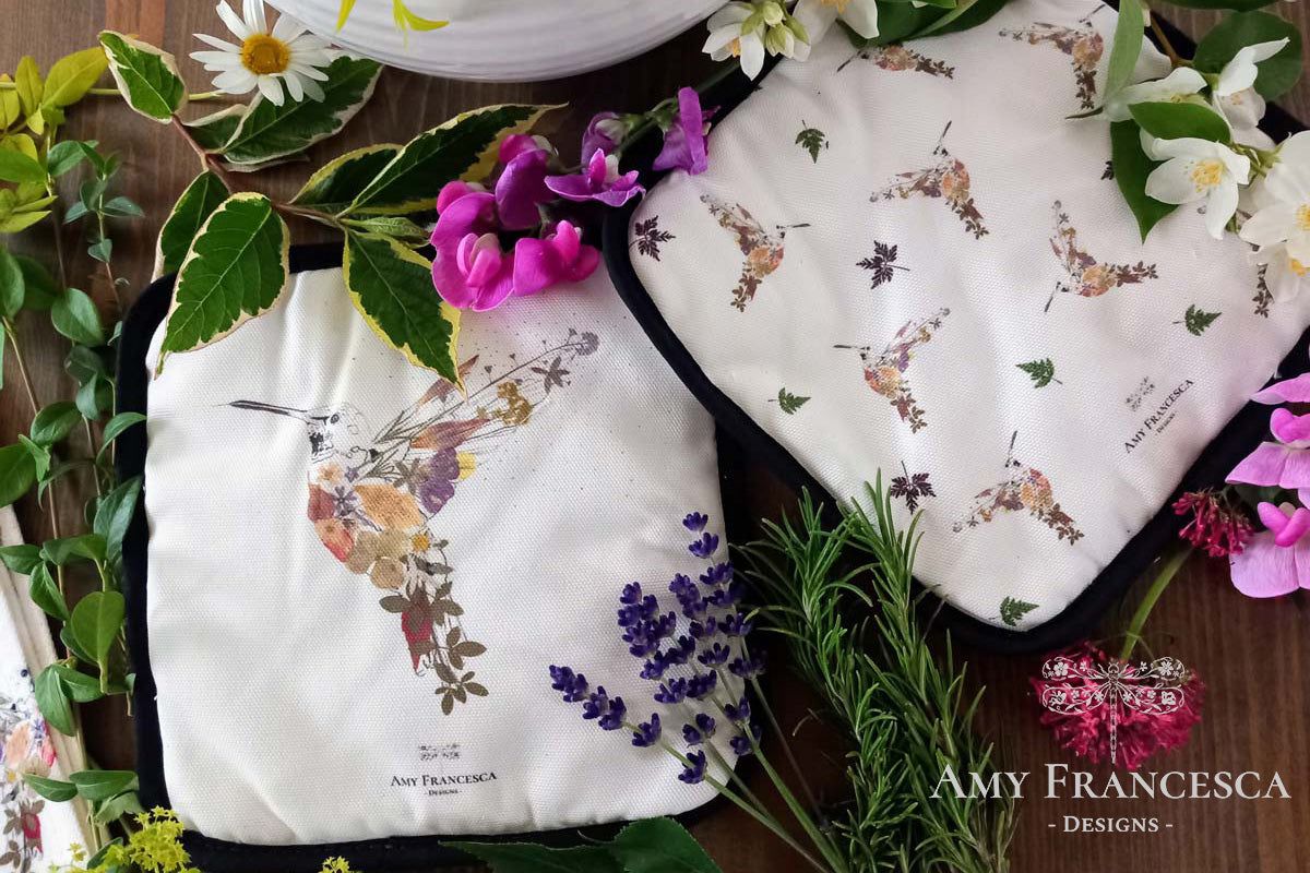 Two pot holders featuring hummingbird illustrations, shown with surrounding flowers and greenery.