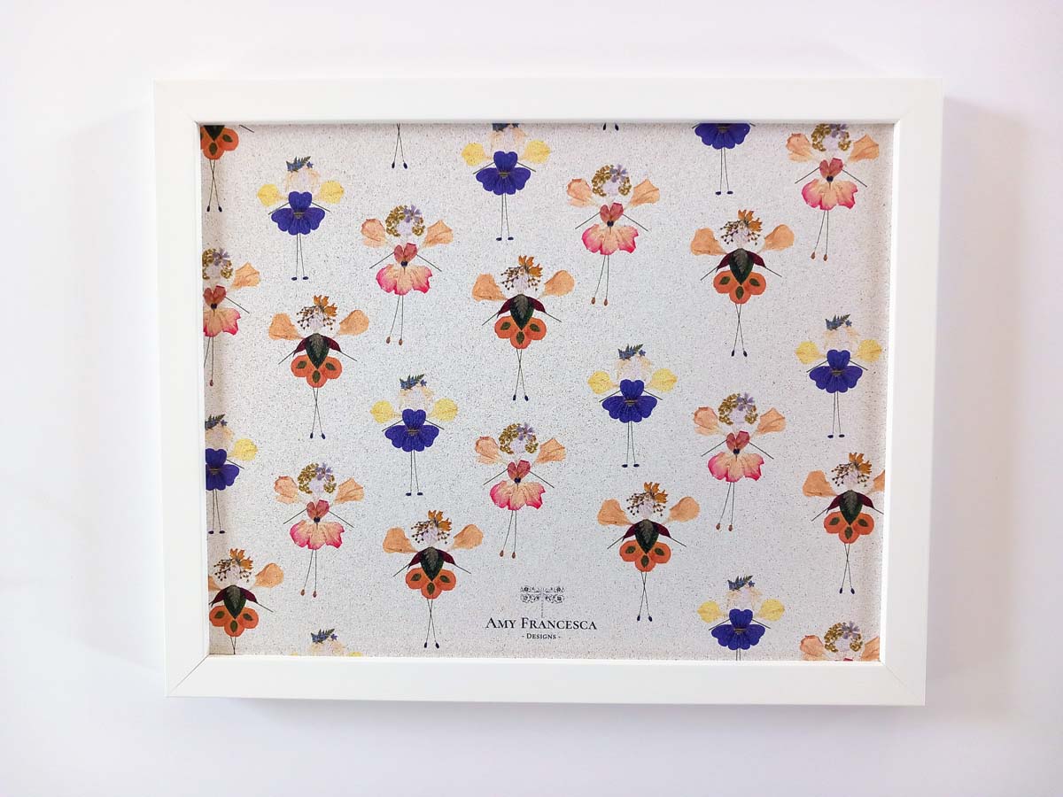 Framed cork pin board featuring a repeating pattern of small floral figures on a light background.