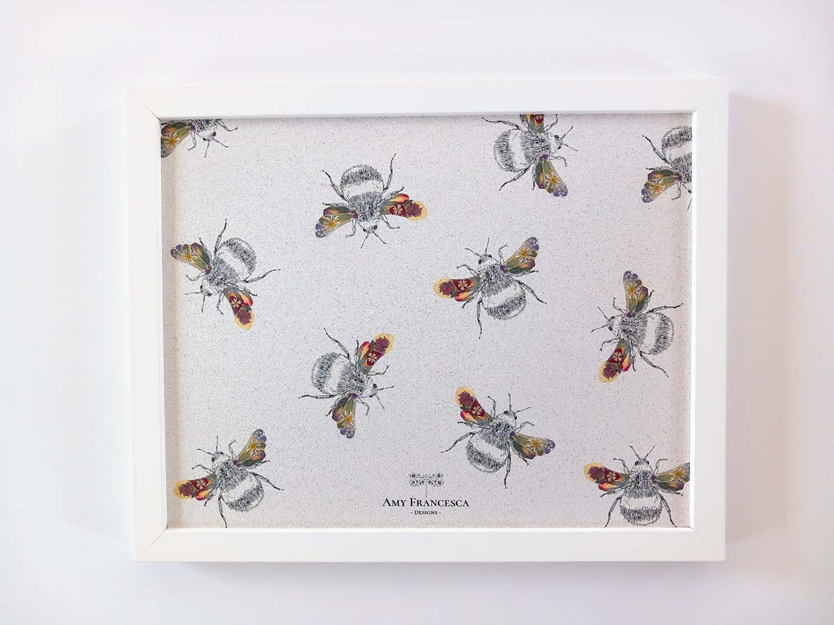 Framed cork pin board featuring a bee illustration in a random repeat on a light background.
