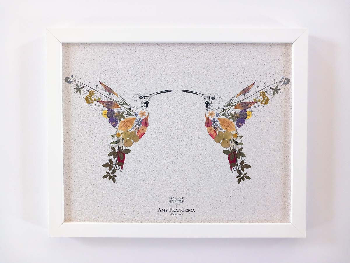 Framed cork pin board featuring two hummingbirds facing each other on a light background.