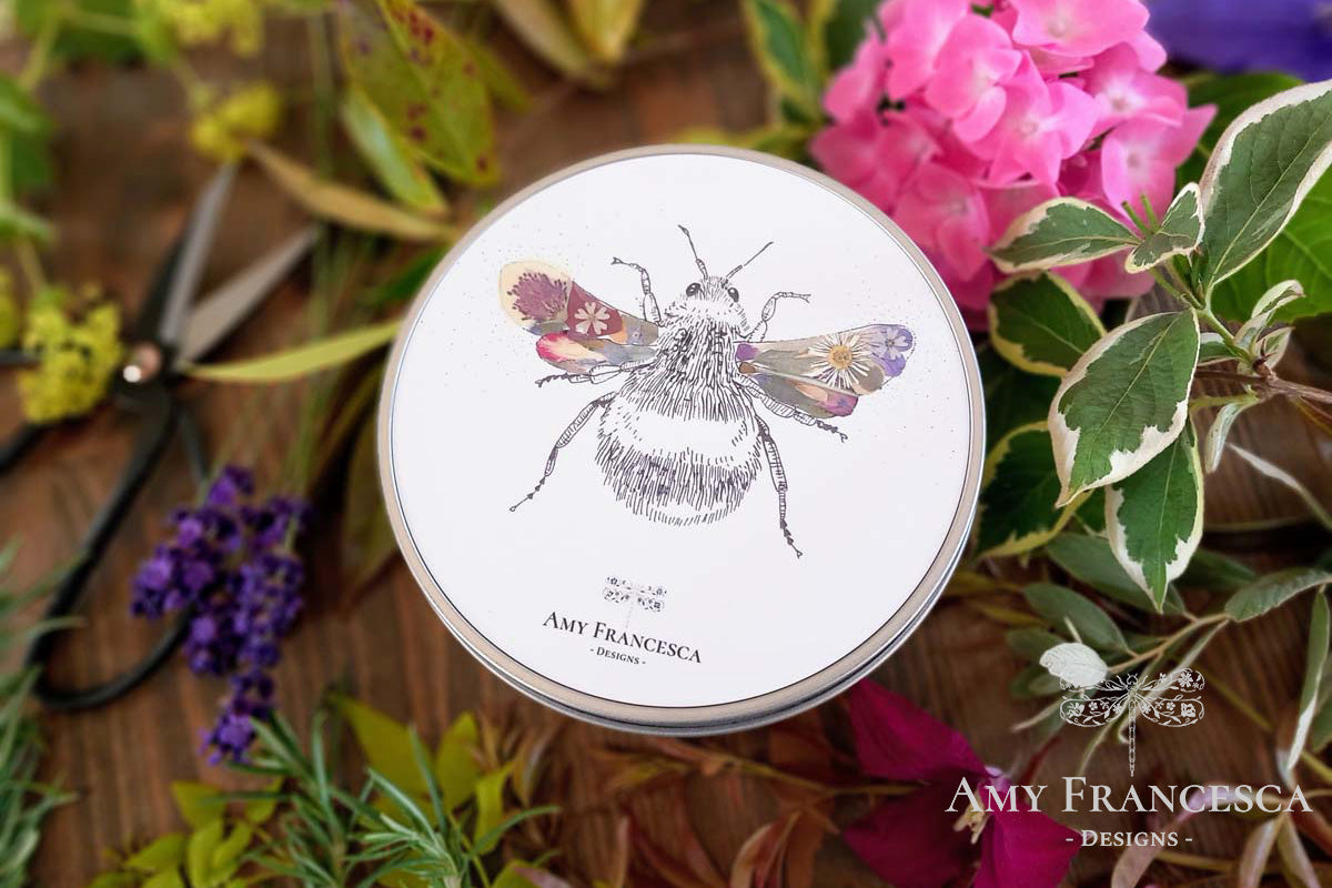 Round storage tin featuring a bee illustration, shown with surrounding flowers and leaves.
