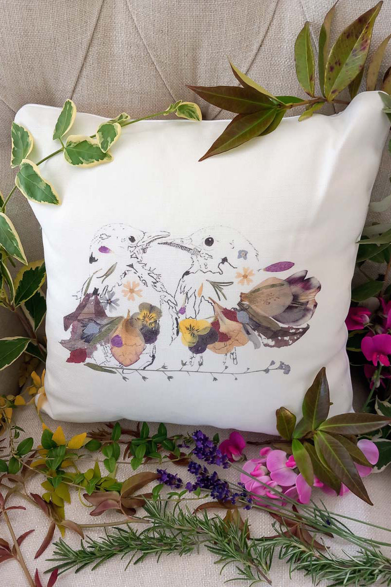 Cushion featuring an illustration of two birds on a branch, surrounded by assorted flowers and leaves.