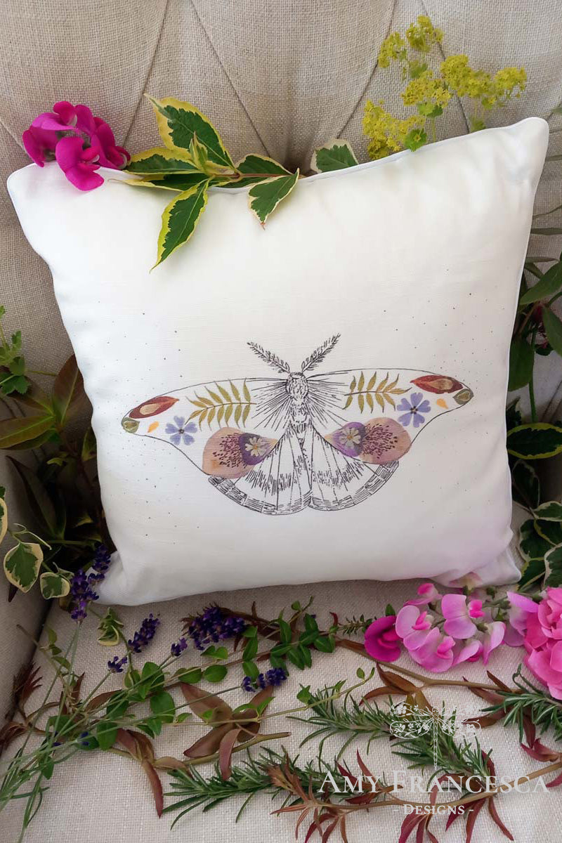 Cushion featuring a moth illustration, shown on a chair with surrounding flowers.