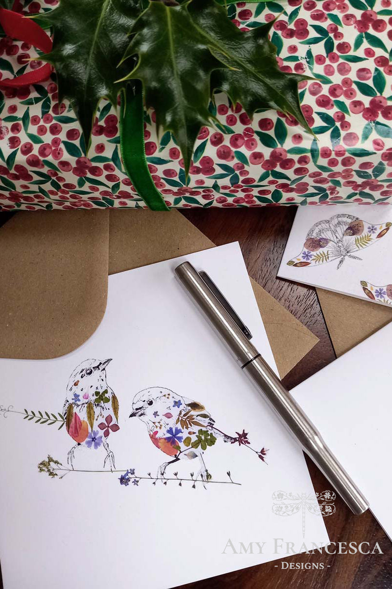 Greeting cards featuring a bird illustration and a moth illustration, shown with envelopes, a wrapped gift and a pen.