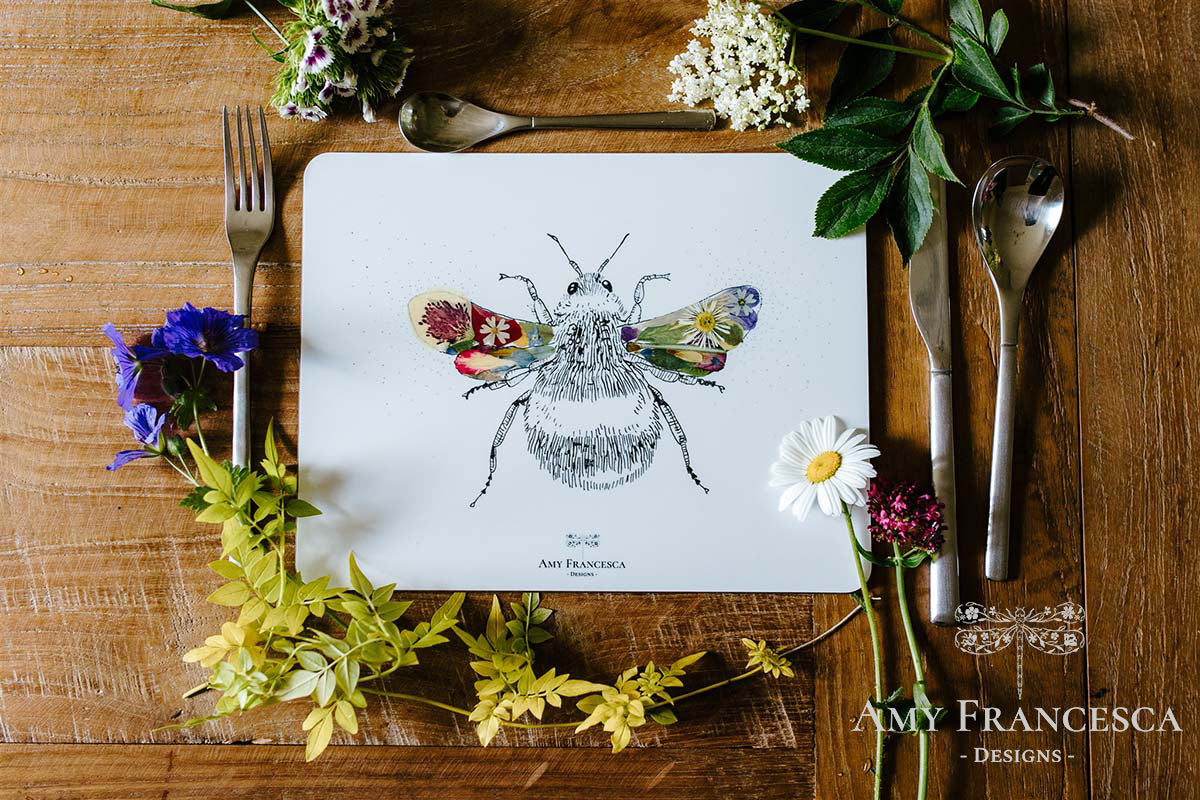 Placemat featuring a bee illustration, shown with cutlery and assorted flowers.
