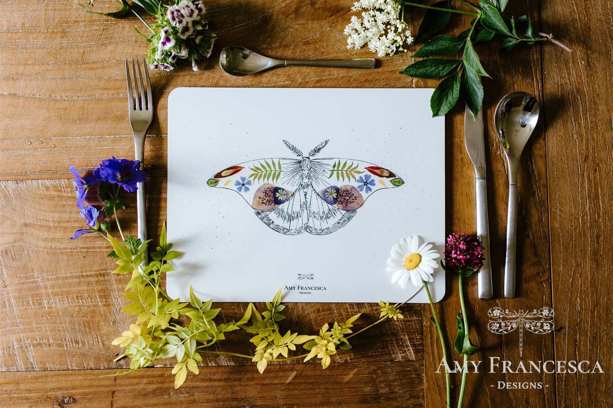 Placemat featuring a moth illustration, shown with cutlery and surrounded by flowers and greenery.