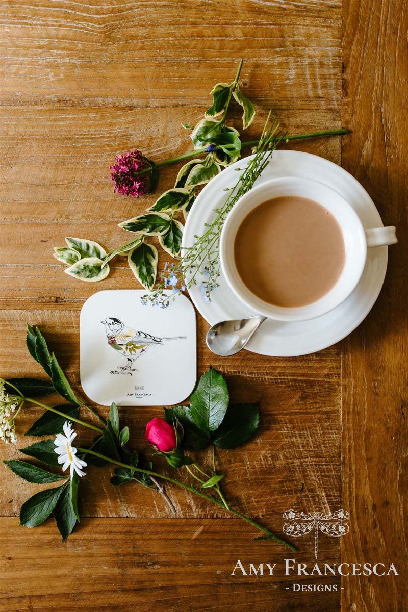 Coaster featuring a bird illustration, shown beside a cup and surrounding flowers.