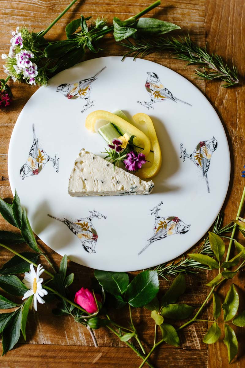 Serving platter with bird illustrations, shown with food and surrounded by herbs and flowers.