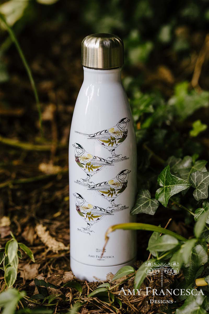 White water bottle featuring four bird illustrations, photographed among green leaves.